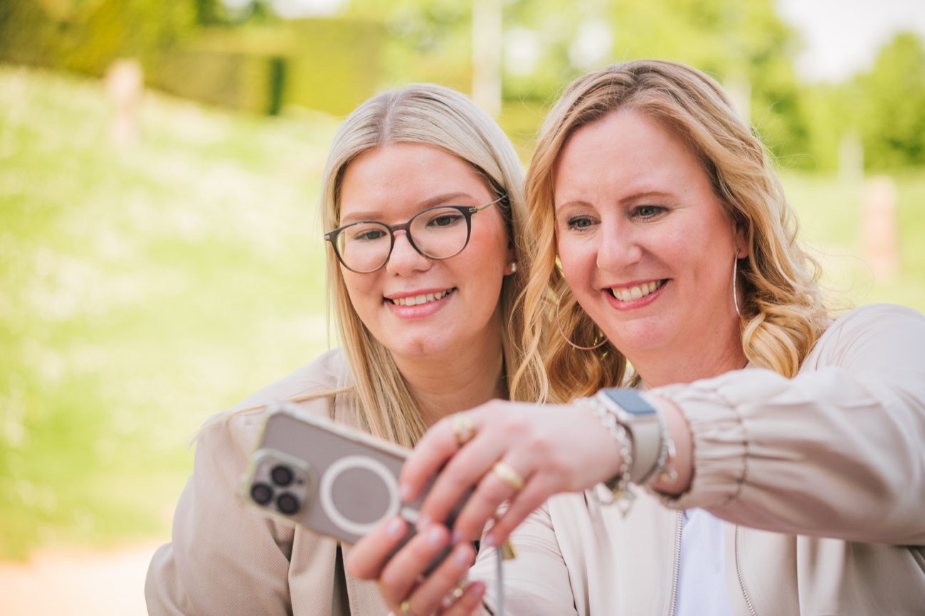 Sina Waris Hülk und Doris Greinert lachen gemeinsam beim Blick auf ein Smartphone